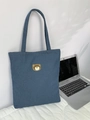 Dettaglio del ricamo a forma di orso su borsa in denim blu accanto a un laptop - Orso Ricamato / Azzurro