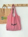 Detail van rood-wit geblokte canvas draagtas met zwarte Peachy tekstbedrukking - Rode Ruit (Peachy Zwarte Letters)