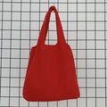 Detail of red canvas tote bag hanging on a grid background showing durable fabric texture - Red
