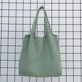 Detailed view of light green canvas tote bag hanging on a industrial black mesh wall - Light Green