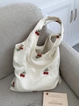 Gros plan sur la broderie cerise du sac en toile beige posé sur un canapé gris doux - Sac Gilet à Broderie Cerise