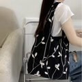 Black canvas tote bag with white leaf embroidery worn by a model in a cozy home setting - Black with Embroidery