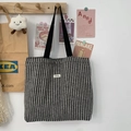 Detail of black and white herringbone wool tote bag with brand label on a wooden hook - Woolen Stripe Black