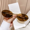 Retro oval sunglasses with thin gold metal frame and brown lenses held by a model - Gold Frame Brown Lens