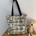 Grande borsa tote in tela beige con scritte cinesi e manici in nylon nero su un tavolo - Rifiuta l'ansia