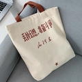 Détail du sac cabas en toile avec étoile rouge et calligraphie sur un canapé gris - Blanc Cassé Slogan (Abandonner les Illusions)