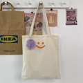 Detail van de minimalistische canvas shopper met oranje smiley en paars pluche hangertje - Beige (Met Hanger)