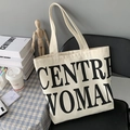 Detail of minimalist cream canvas tote bag with black CENTRE WOMAN text on a chair - CEN Letter / Beige