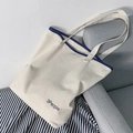 Minimalistische cremeweiße Canvas-Tragetasche mit dunkelblauem Rand auf dem Sofa - People Beige Tasche (H66998554)