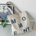 Minimalist cream canvas tote bag with MOMENT print and wide straps in lifestyle setting - Beige MOMENT Letter Style