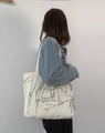 Vista lateral de bolso tote de lona blanca con líneas abstractas usado al hombro - Bolso beige con líneas artísticas