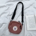 Vista plana de un bolso bandolera de lona rosa palo con parche de dibujos en fondo blanco - Rojo Pasta de Frijoles