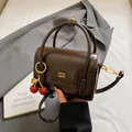Detail of vintage dark brown handbag with gold logo and cherry charm on grey fabric - Coffee