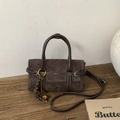 Detail einer dunkelbraunen Wildledertasche mit weißen Nähten und Zieranhängern auf Holz - Braun