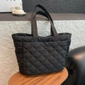 Quilted black tote bag with diamond stitching displayed on a wooden side table - Black