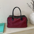 Minimalist two-tone leather Boston bag in black and burgundy on a stone pedestal - Red