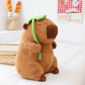 Capybara plush toy with green leaf on head sitting on bed in cozy home setting - 50cm, 1.1kg / Capybara with Lotus Leaf