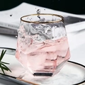 Hexagonal glass tumbler with gold rim filled with pink drink and splashing ice cubes - Gold Rimmed Hexagonal Cup