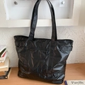 Large black tote bag with front zipper pocket and glossy texture on a light wood desk - Black