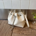Detail view of white drawstring bucket bag with silver chain on wooden surface - Off White
