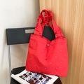 Red pleated tote bag with silver metal studs and drawstring closure on a black chair - Red