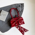 Rote Lackleder-Handtasche mit silbernen Nieten und Schleife auf grauem Blazer - Rot