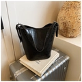 Détail du sac seau noir à motif crocodile posé sur un livre et une valise argentée - Noir