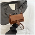 Detail of lychee pattern leather handbag with white contrast stitching on a bed - Brown