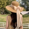 Elegant beige straw sun hat with long ribbon bow shown on model in a sunny park - Big Streamer Ribbon Kaka