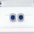 Detailed close-up of oval sapphire halo earrings with micro-paved diamonds in a gift box - Blue Stud Earrings