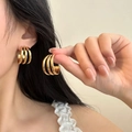 Detail of three-layered gold titanium steel hoop earrings worn on female ear model - 25mm / Simple C-Shaped Hoop (PJER254) / Gold