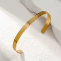Close-up of a minimalist golden stainless steel open cuff bracelet on white stone - Gold Open Cuff Bangle