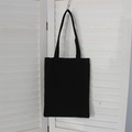 Detail view of a thick black canvas tote bag hanging against white shutters - Black (8oz)