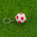 Gros plan du mini porte-clés football rouge et blanc sur un fond de pelouse verte - Rouge