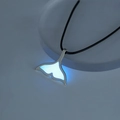Detailed view of a whale tail pendant with bright blue glow in the dark effect on black cord - Blue-Green Fishtail (NY934)