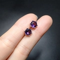Macro view of purple round-cut zircon earrings with silver six-prong settings on hand - Purple Rhinestones
