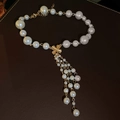 Elegant white pearl tassel necklace set with a golden clover pendant on leather background - Pearl Tassel Necklace
