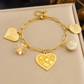 Goldenes Gliederkettenarmband mit Herz-, Blumen- und Sonnenanhängern auf beigem Ständer - Armband / B2076