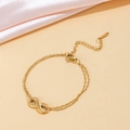Close-up detail of a gold-toned infinity charm on a delicate double-strand chain bracelet. - Infinity Symbol (110) / Gold