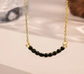 Detail shot of a curved gold smile necklace inlaid with shimmering black gemstones - Black Zirconia (Gold Necklace)