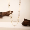 Detalle de un collar de perlas barrocas a capas con cadena dorada sobre fondo minimalista - Perla Redonda (QYH1073)