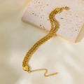 Detalle de una pulsera de triple cadena de cuerda dorada sobre una superficie de piedra - Pulsera de Cadena Trenzada de Triple Capa (E2056) / Dorado