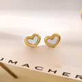Dettaglio macro di orecchini a cuore dorati con inserto in madreperla su cartoncino - Orecchini a Cuore in Madreperla Bianca (QYG217)