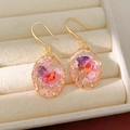 Detailed view of handmade resin earrings with dried pink flowers in a gold setting - Oval Teardrop / Pink Ear Hook