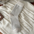 Gemütliche Wollsocken in Creme mit grauen Streifen auf Zopfstrick-Hintergrund - Beige