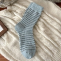 Gemütliche blau-grau gestreifte Wollsocken mit Rippbündchen auf weißem Strickhintergrund - Hellblau