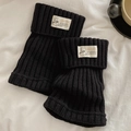 Black knitted leg warmers with vintage label on soft white fabric background - One Size / Black