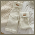 Cozy cream white ribbed knit leg warmers with retro leather brand label on bed sheet - One Size / Cream