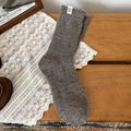 Dark grey knitted wool socks with a white label on a cozy wooden background - Rolled Edge Coffee