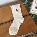 Beige Christmas crew socks with brown reindeer embroidery on a cozy wooden background - Cream Reindeer